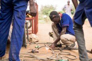 a man in Uganda welds surrounded by other young men